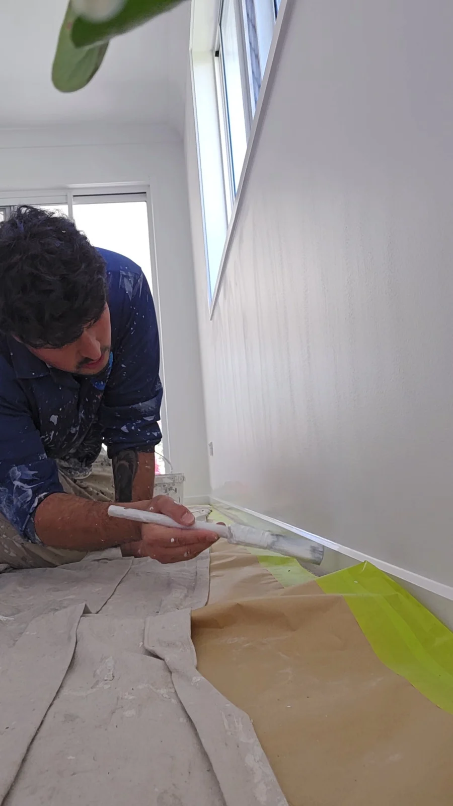 Painter brushing skirting beside protected flooring